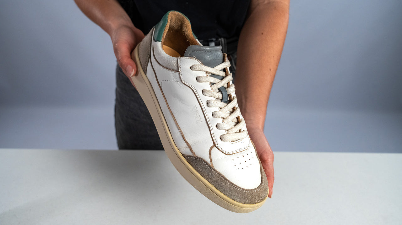 worn out pair of the hedonist white grey green sneakers being held by a man after being cleaned