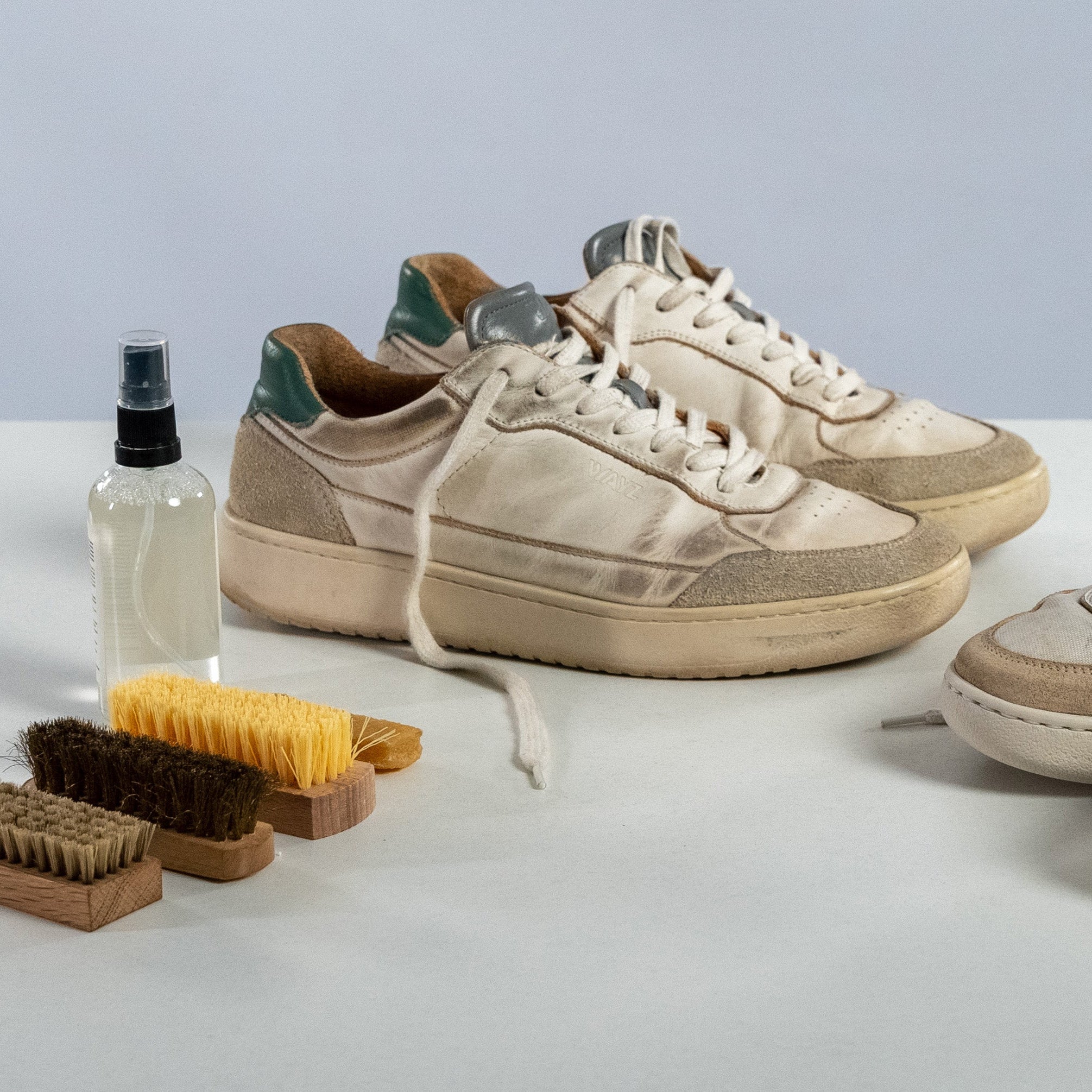 a worn out pair of the hedonist white grey green sneakers and a worn out pair of the sonder white grey dry rose sneakers next to several different brushes 
