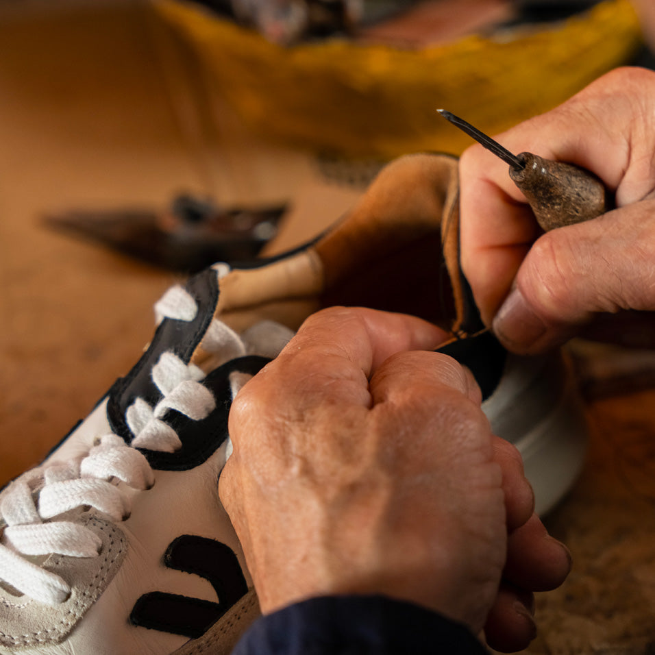 a cobbler repairing an open seam on a pair of the misfit white grey black sneakers at a shoe repair shop