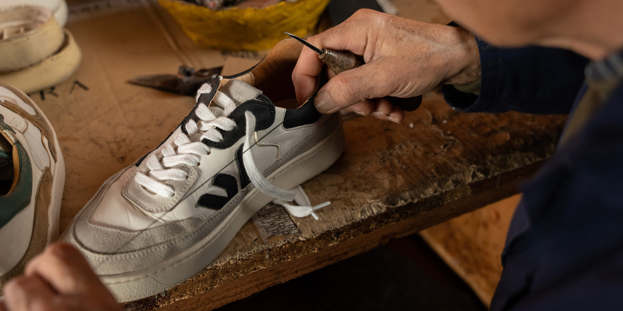 a cobbler repairing an open seam on a pair of the misfit white grey black sneakers at a shoe repair shop