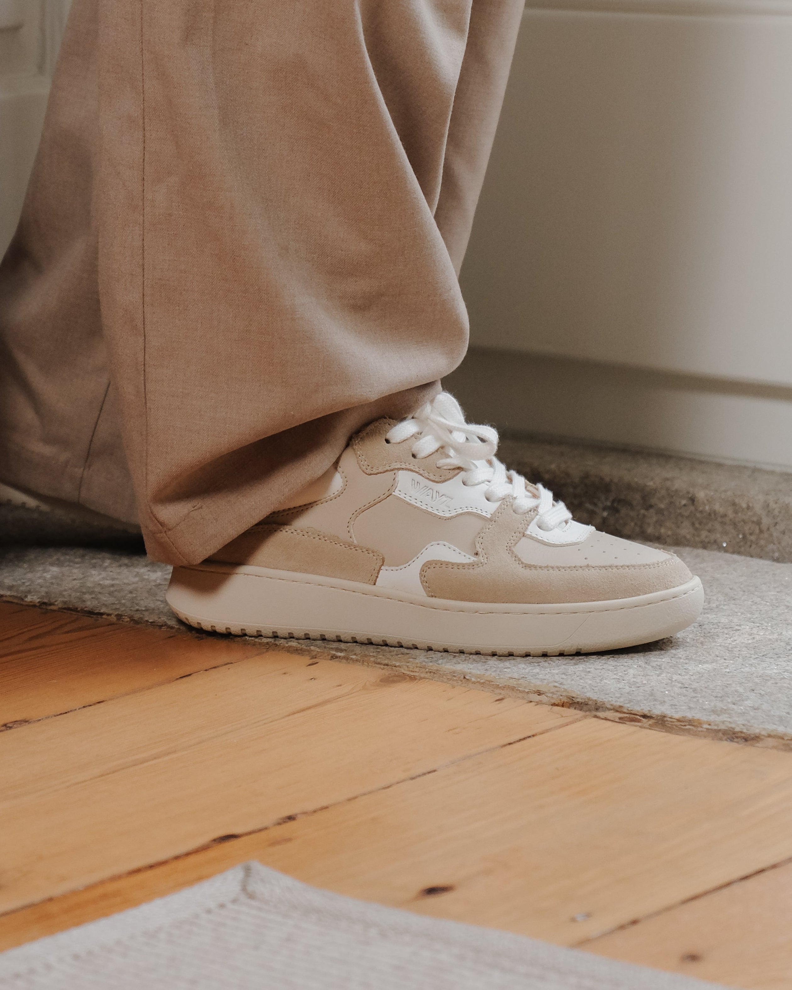 Beige Sonder sneakers with white accents worn with beige pants on a wooden floor.
