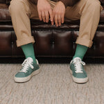 Wayz Grit Pine Green sneakers in front of a couch on carpet