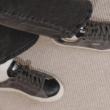 Wayz Grit Anthracite Black sneakers crossed legs stepping on carpet