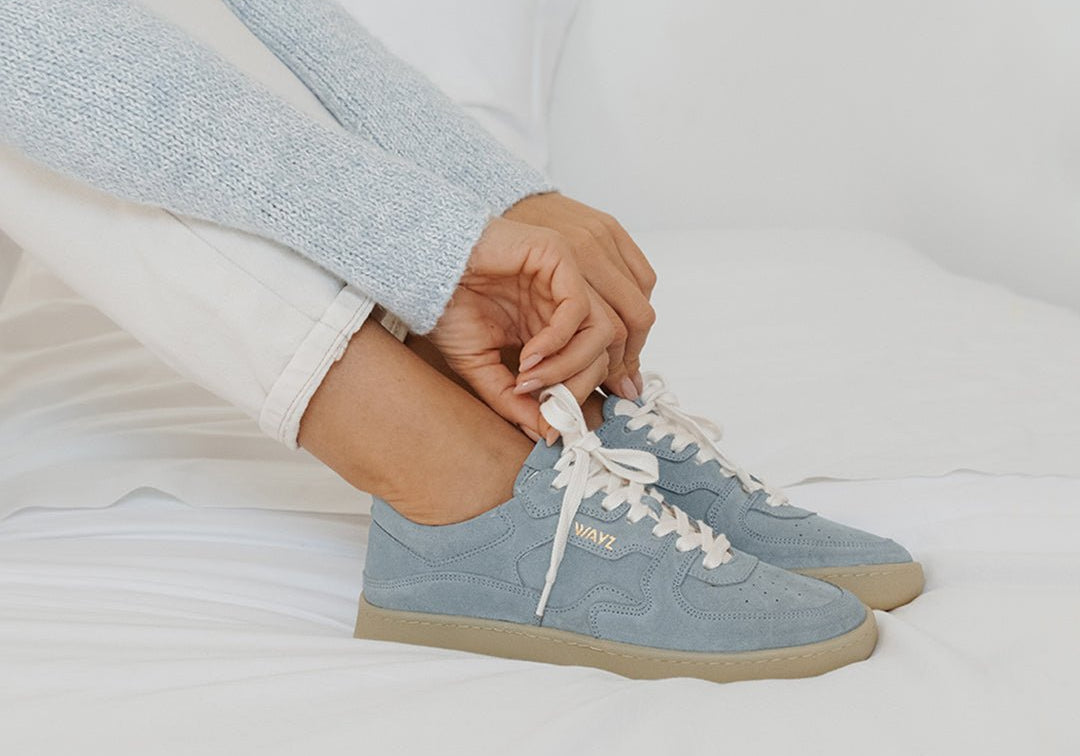 WAYZ Sonder Blue Sky sneakers being laced on top of a bed.