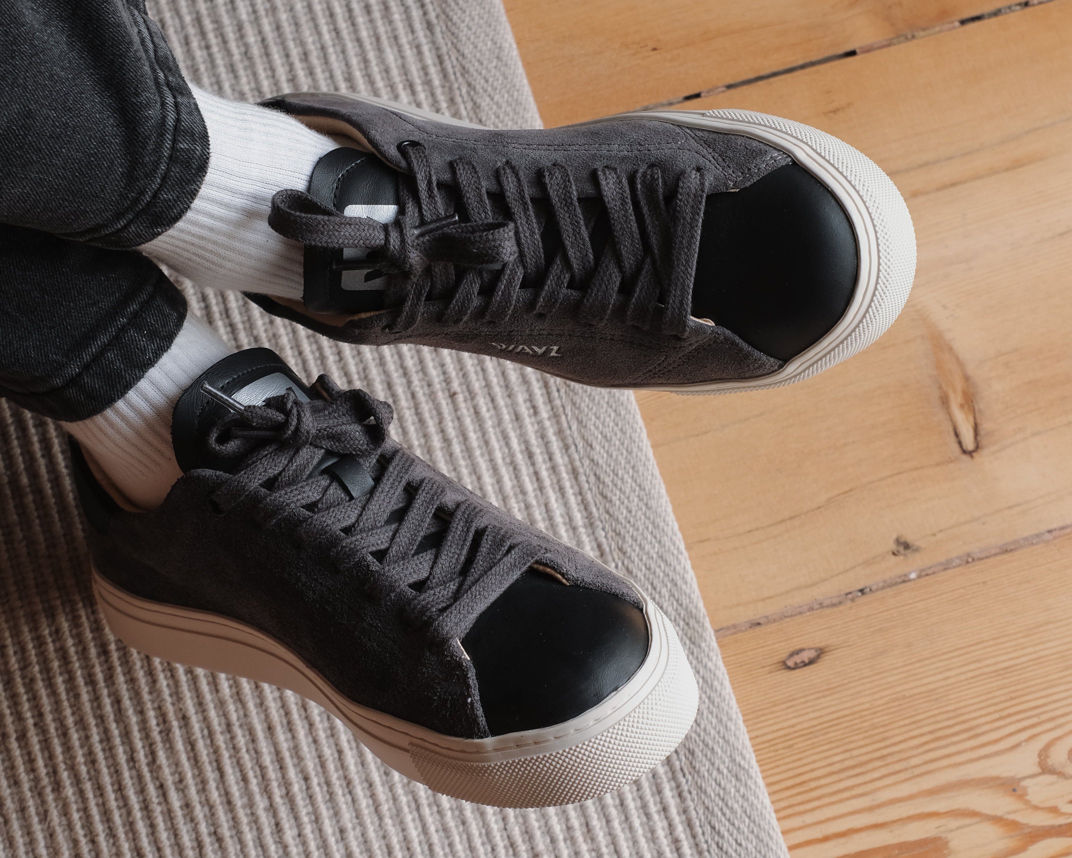Wayz Grit Anthracite Sneakers crossed on top of an carpet in a wood floor